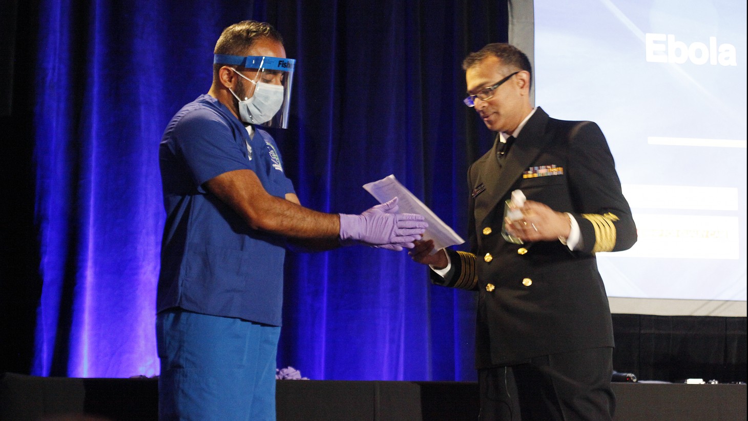 Two health care workers showing protective gear (gloves, mask, face shield)