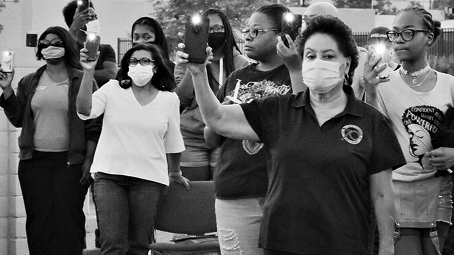 black and white photo with women masked and unmasked holding phone flash lights