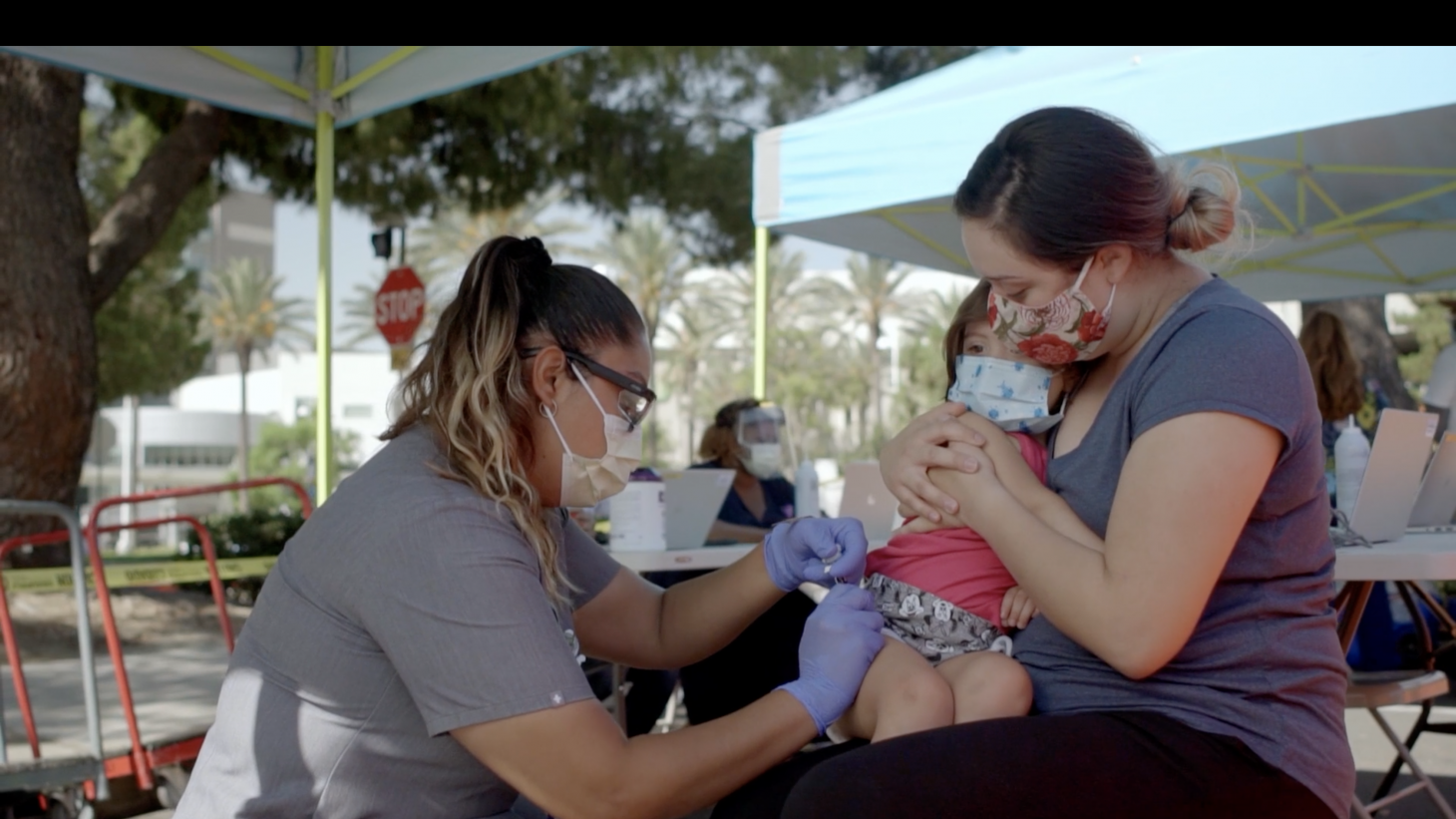 Nurse administers vaccine to child on mother's lap