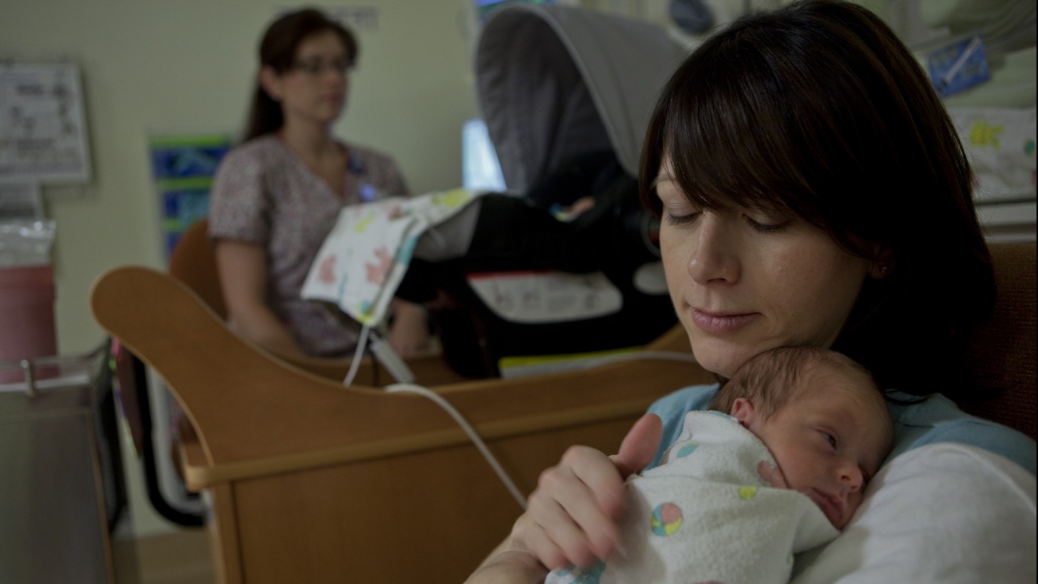 Mother holding her baby, with a nurse in the background 