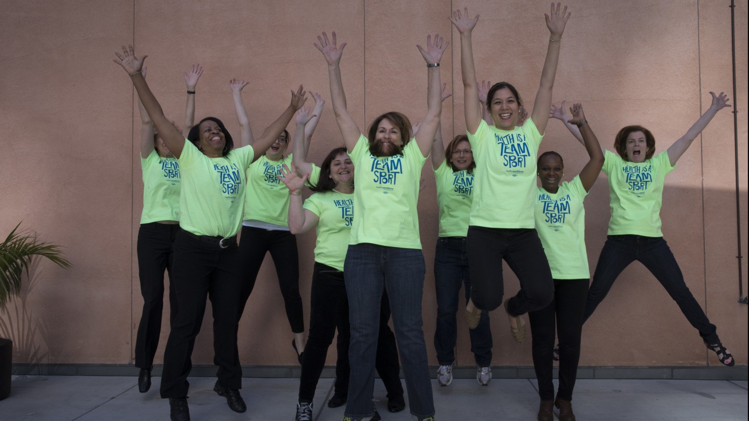 Squad of women in bright green shirts jumping up in the air 