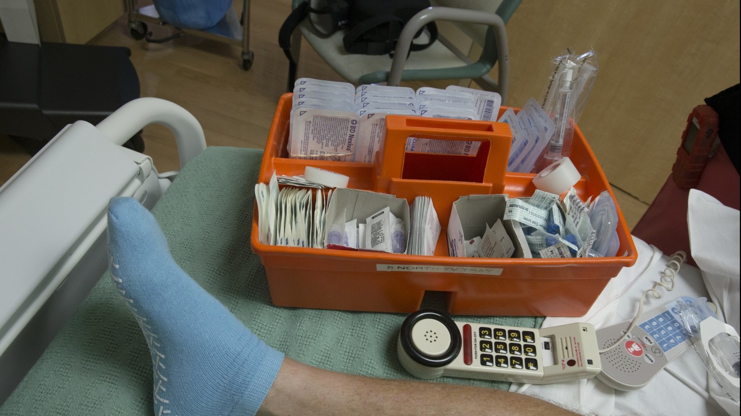 A foot wearing a blue non-slip sock with an orange tray of medical supplies next to it 