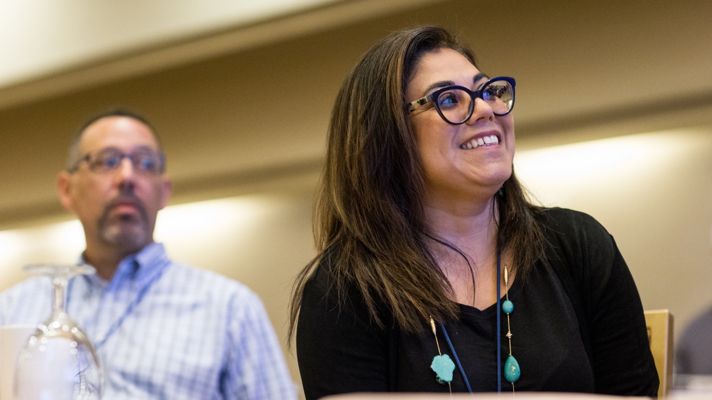 a man in background, a woman in foreground, listening to a presentation